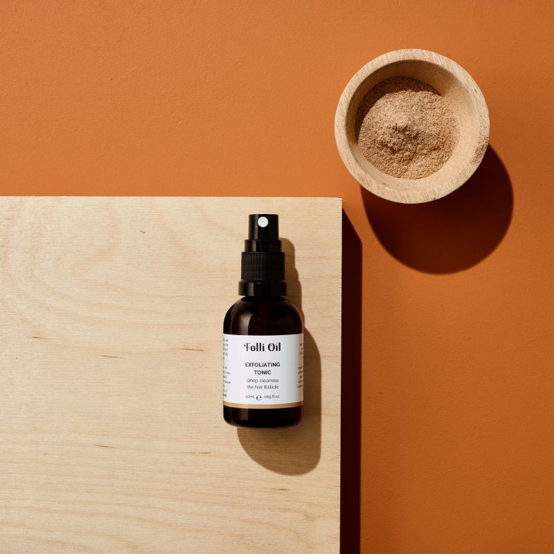 Exfoliating Tonic in amber glass bottle, shown in a flat lay with soft natural lighting – calm, confident skincare.