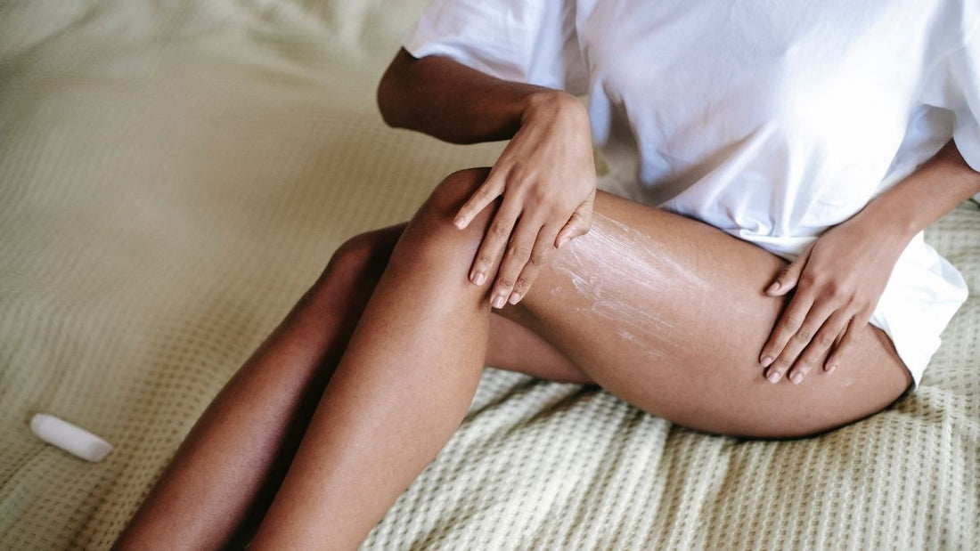 Woman wearing a white t-shirt gently applying moisturiser to her thigh, illustrating a simple, natural skin hydration routine.